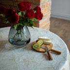 Clear vase with red roses on a table with cheese and kiwi